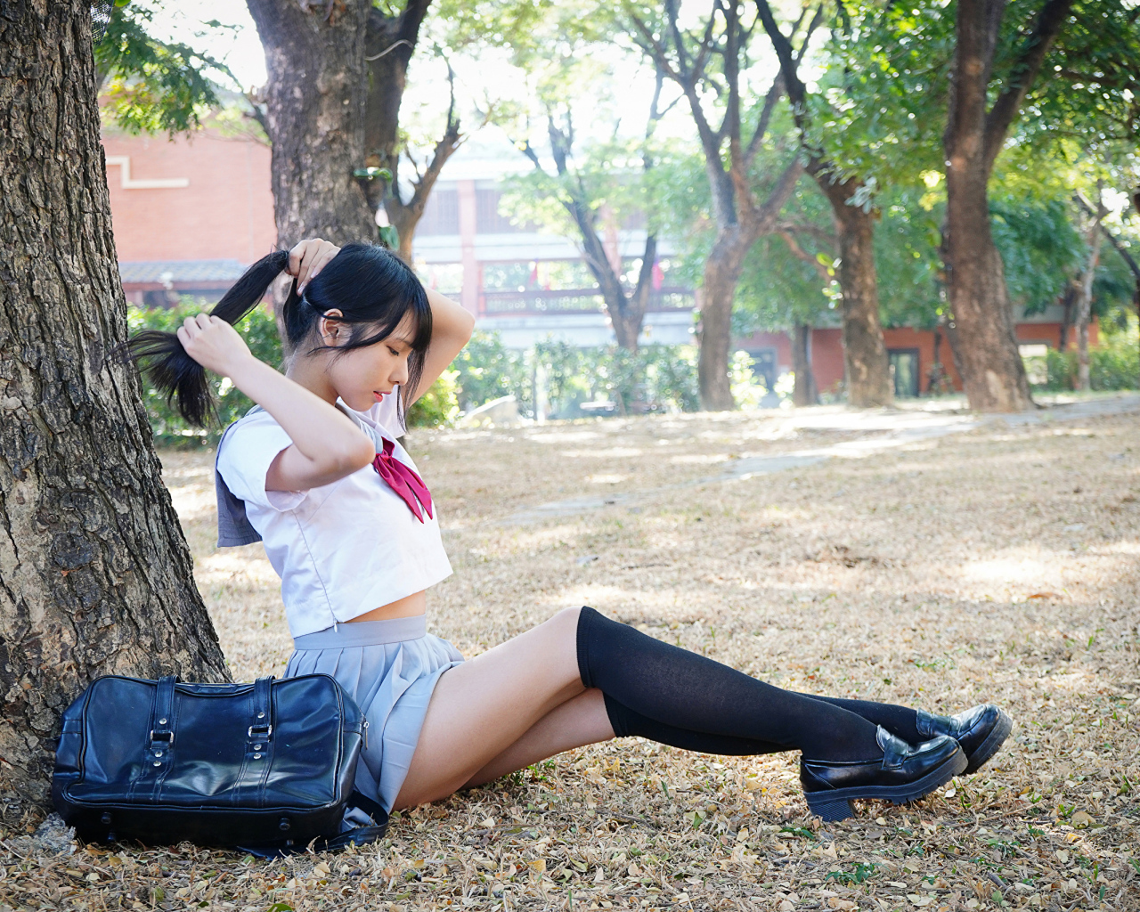 Милая молодая девушка студентка сидит под деревом в парке