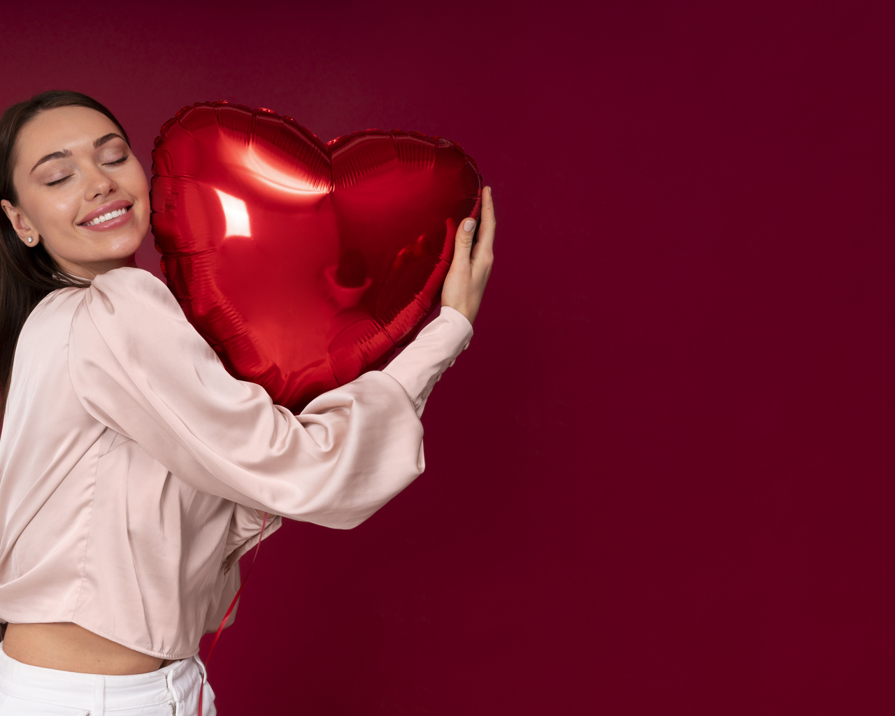 Девушка держит шарик в форме сердца на красном фоне
