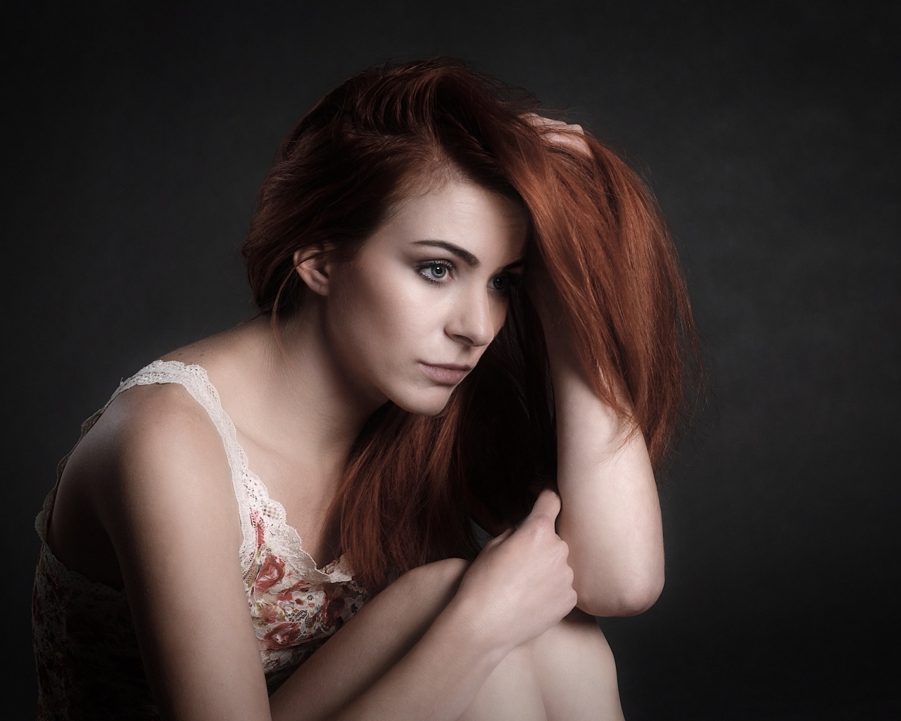 Задумчивая рыжеволосая девушка на сером фоне