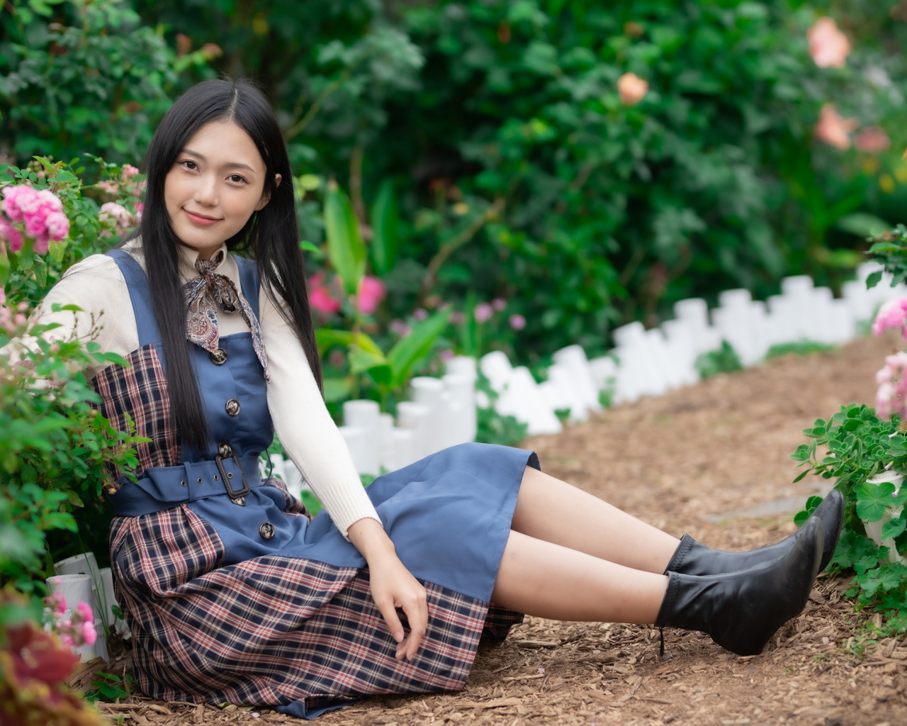Настоящая молодая азиатка сидит на земле у клумбы