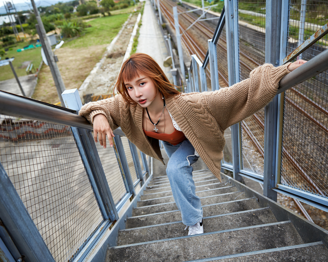 Рыжеволосая азиатка в кофте стоит на ступеньках