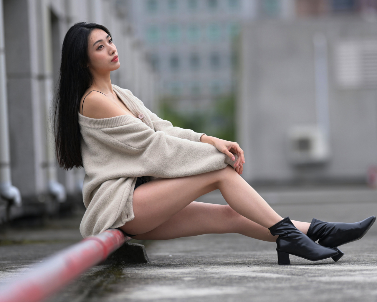 Грустная азиатка в теплой кофте сидит на трубе