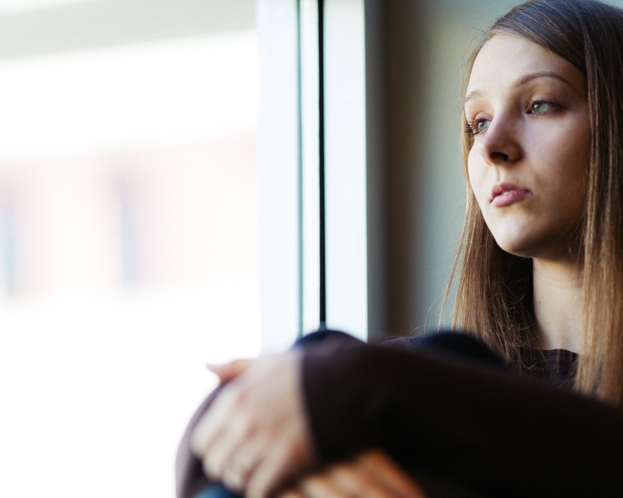 Грустная девушка сидит у окна