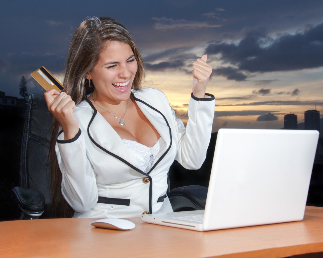 Довольная женщина с карточкой за столом с ноутбуком