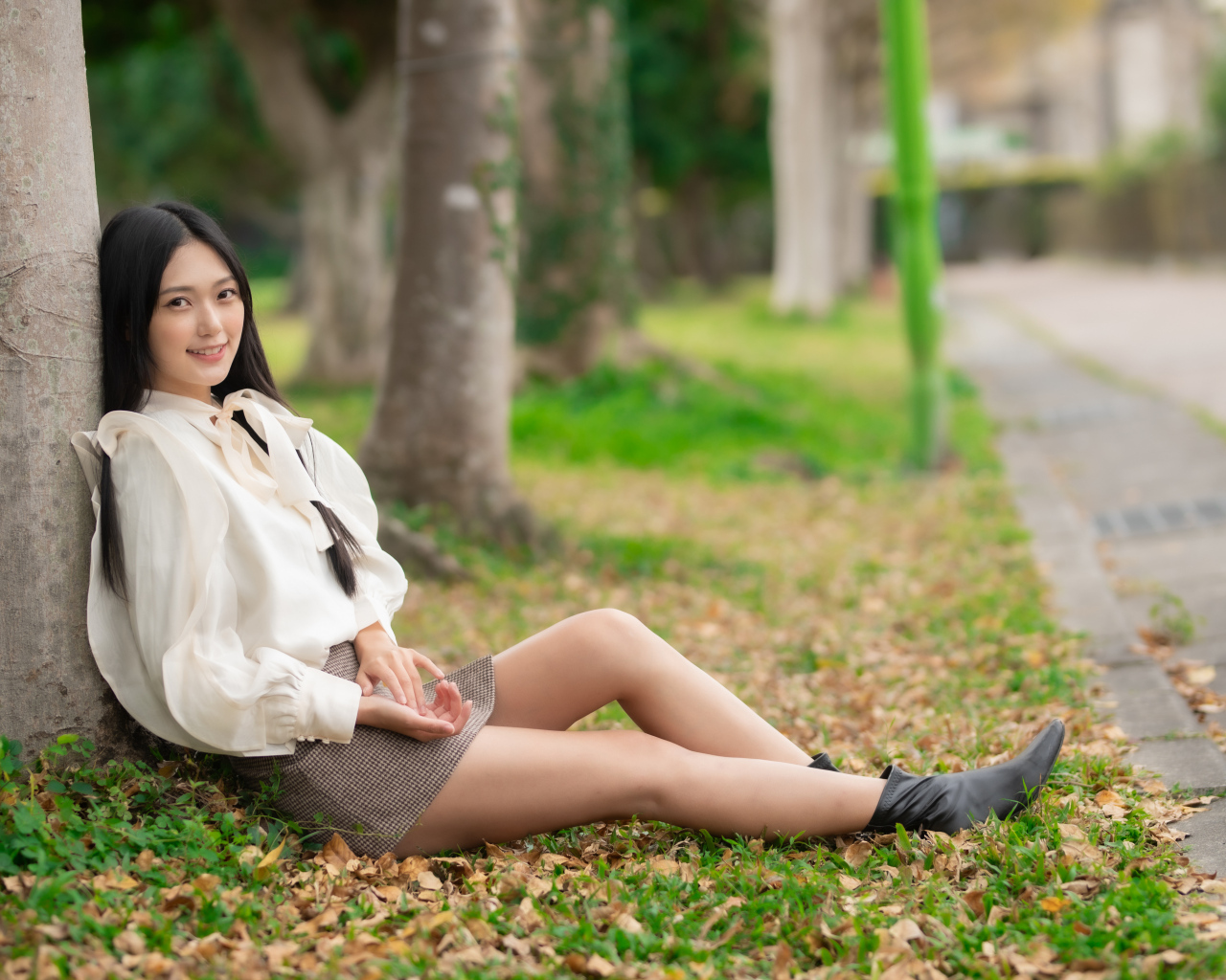 Улыбающаяся азиатка сидит под деревом в парке