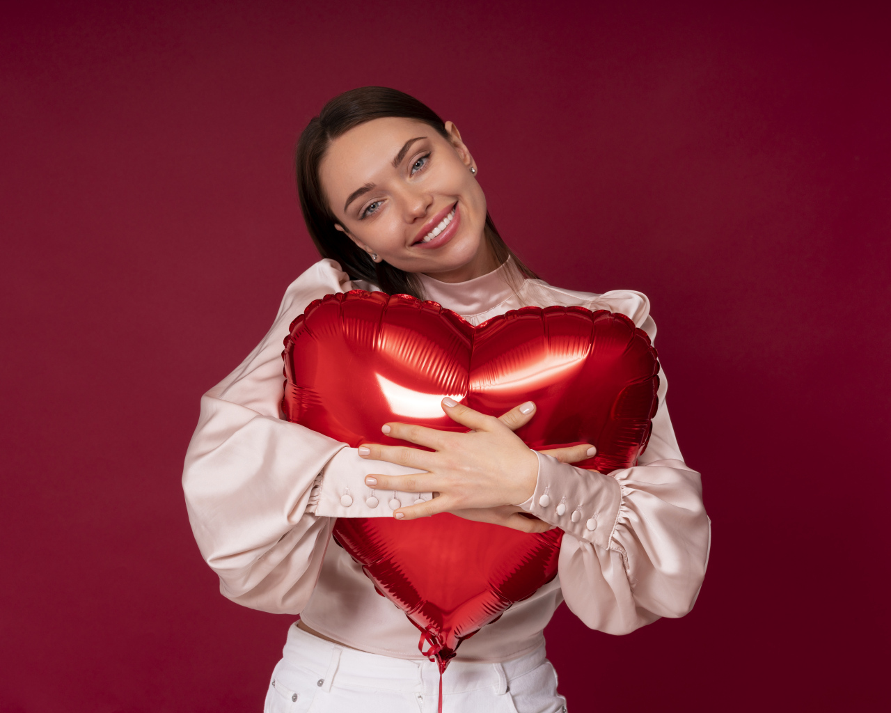 Улыбающаяся девушка обнимает шар в форме сердца