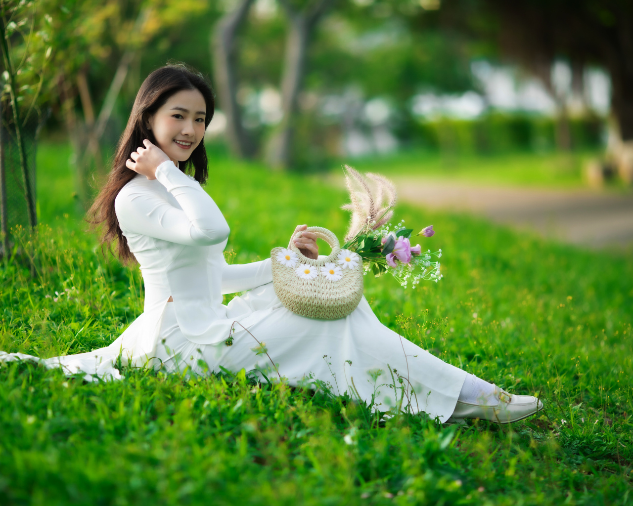 Нежная азиатка в белом наряде сидит на траве