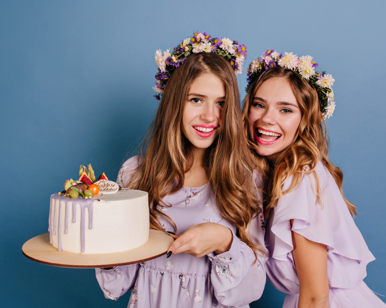 Две веселые молодые девушки с тортом на голубом фоне