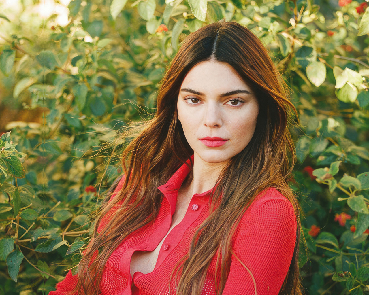 Американская модель Кендалл Дженнер в красной кофте стоит у куста