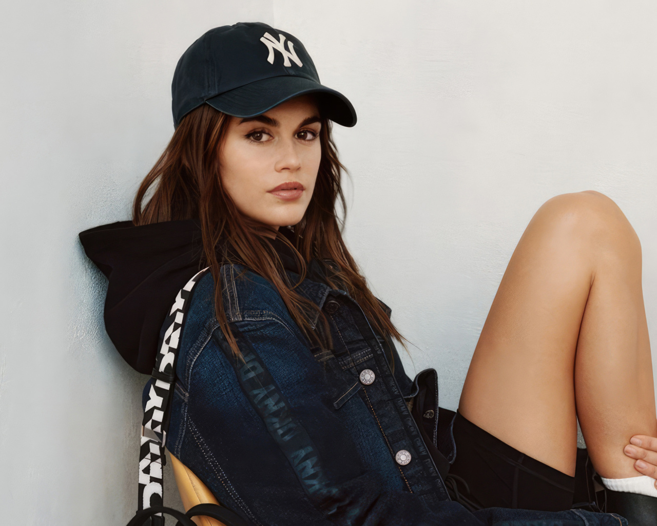 Красивая модель Кайя Гербер в кепке сидит у стены