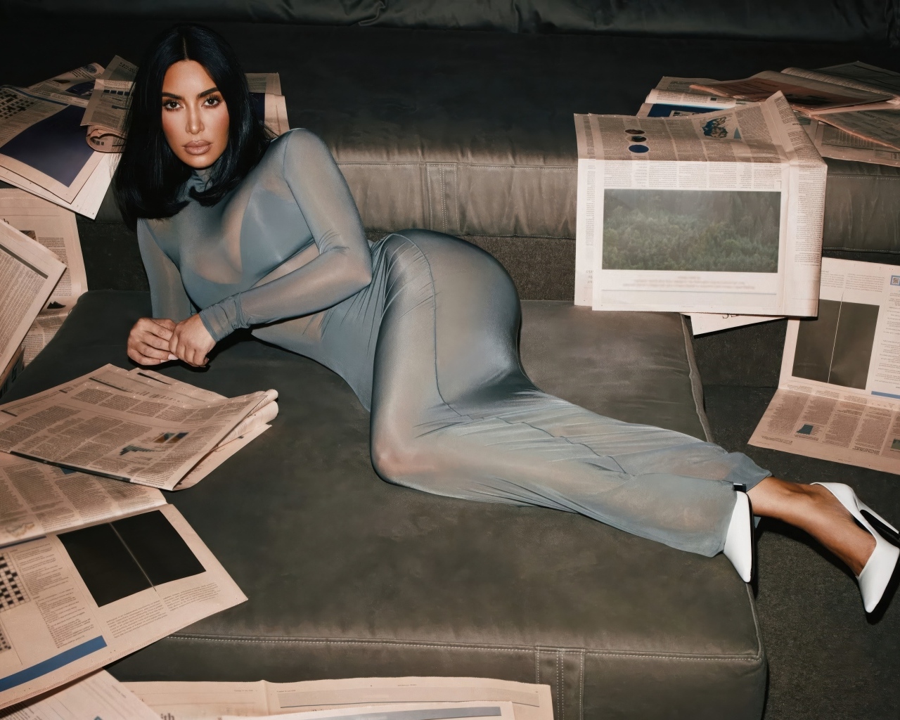Модель Ким Кардашьян лежит на диване с газетами