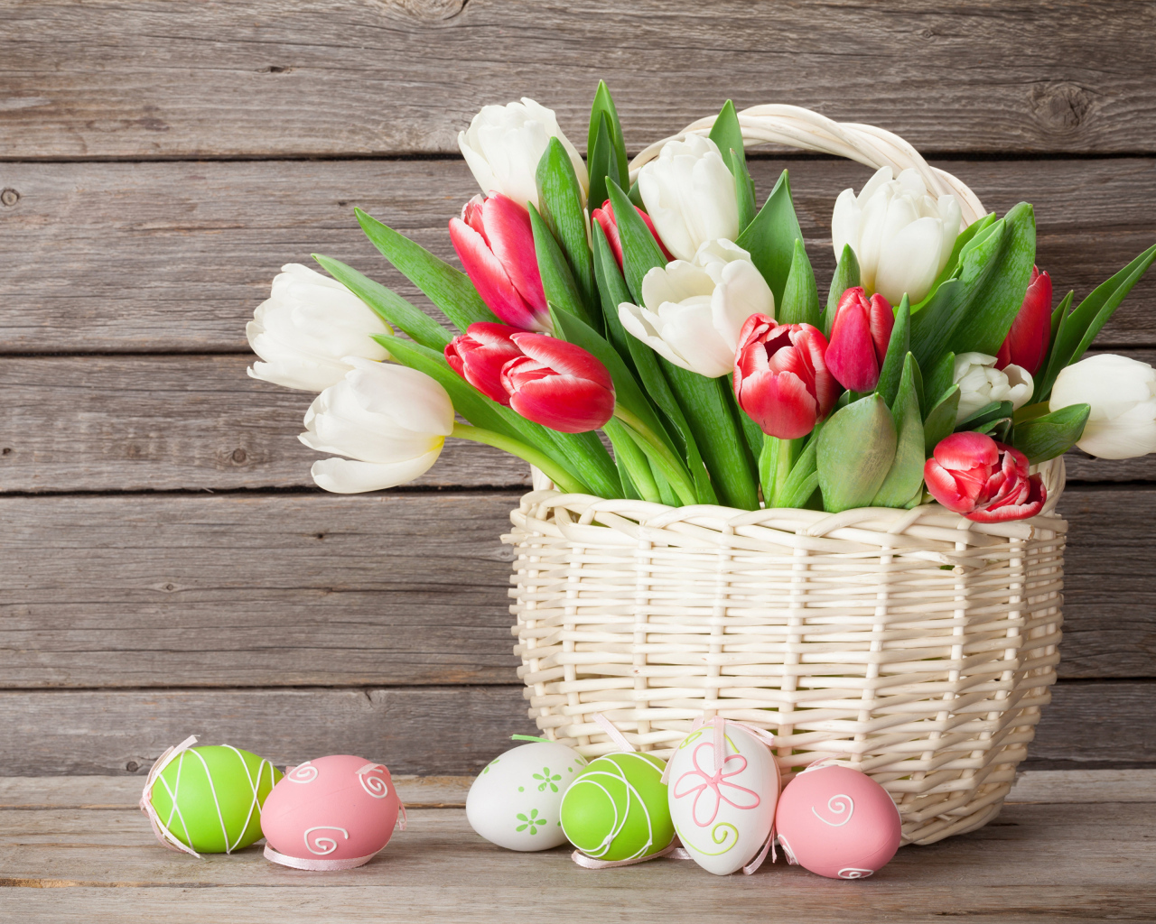 Белые и красные тюльпаны в корзине на столе с разноцветными яйцами на Пасху