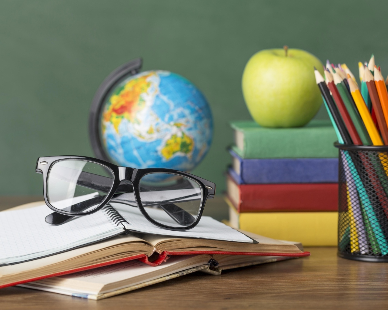 Книги, очки и карандаши с глобусом на столе у доски