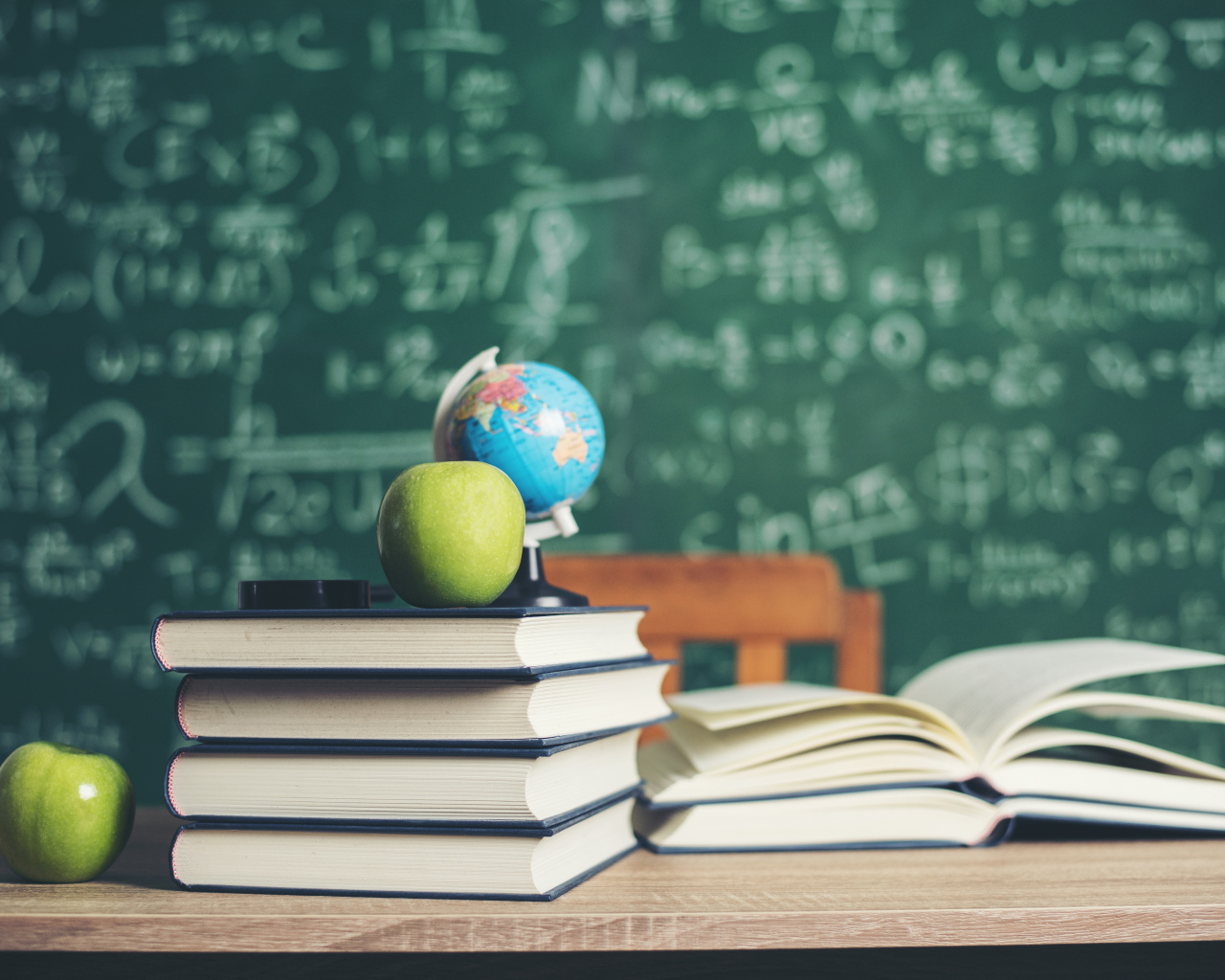Книги на столе с зелеными яблоками и глобусом на фоне доски