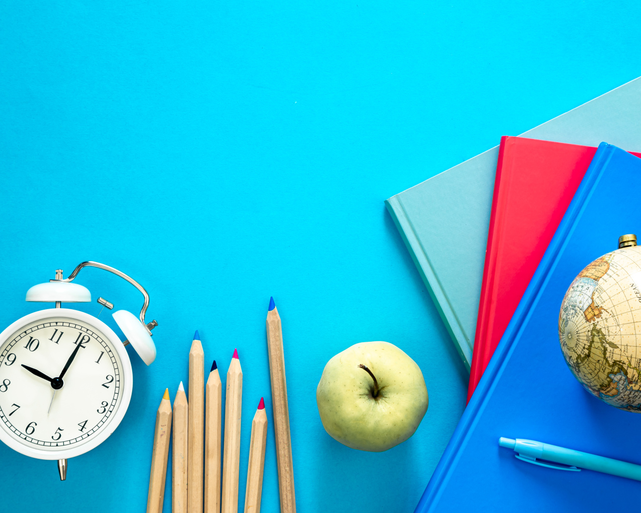 Книги на столе с глобусом, карандашами и будильником