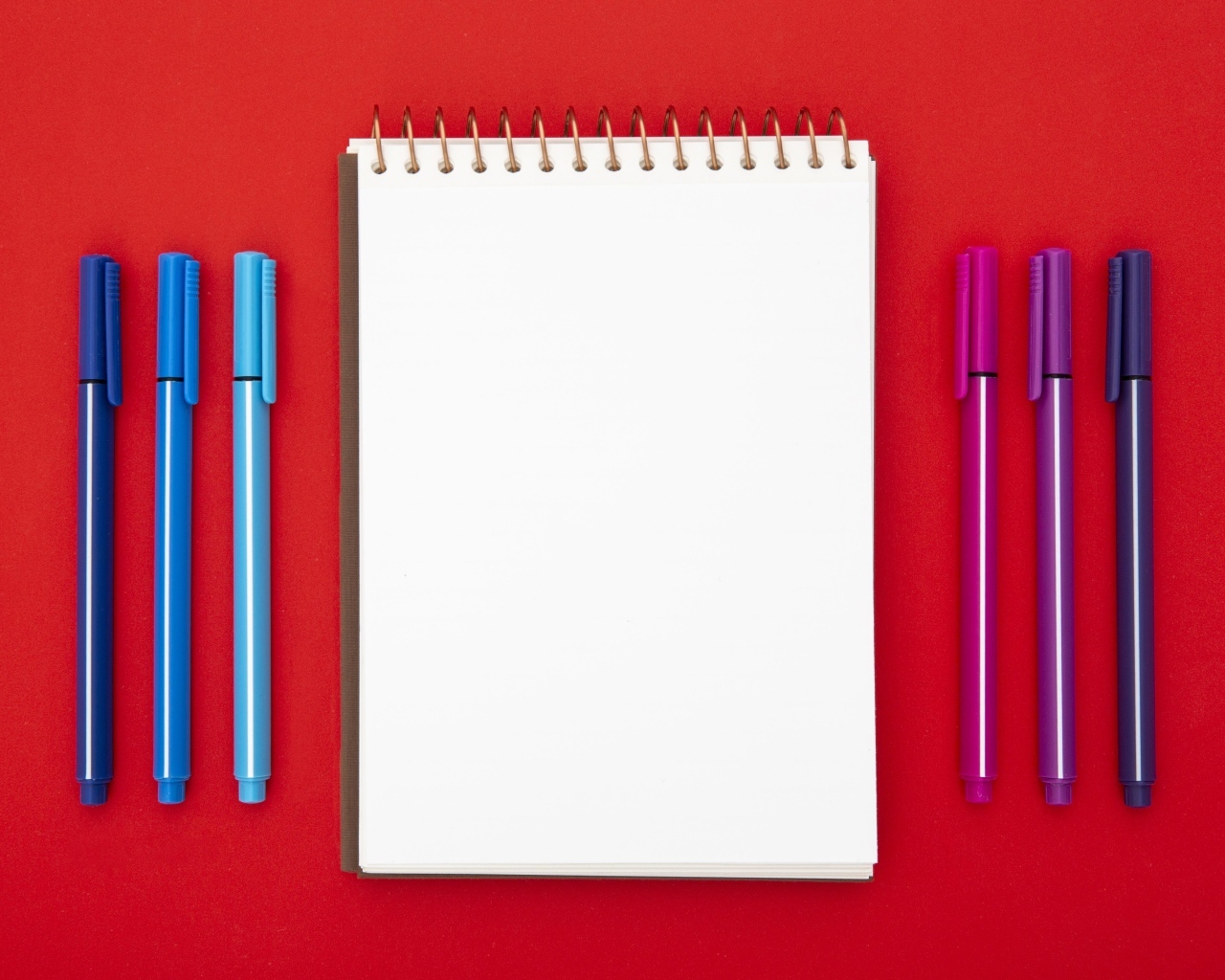 Блокнот и фломастеры на красном фоне