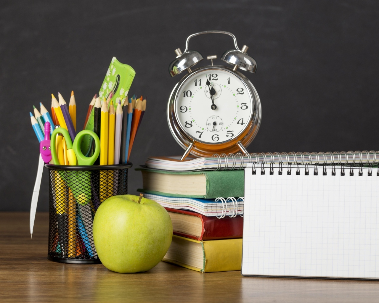 Канцелярские предметы на столе с будильником и книгами 