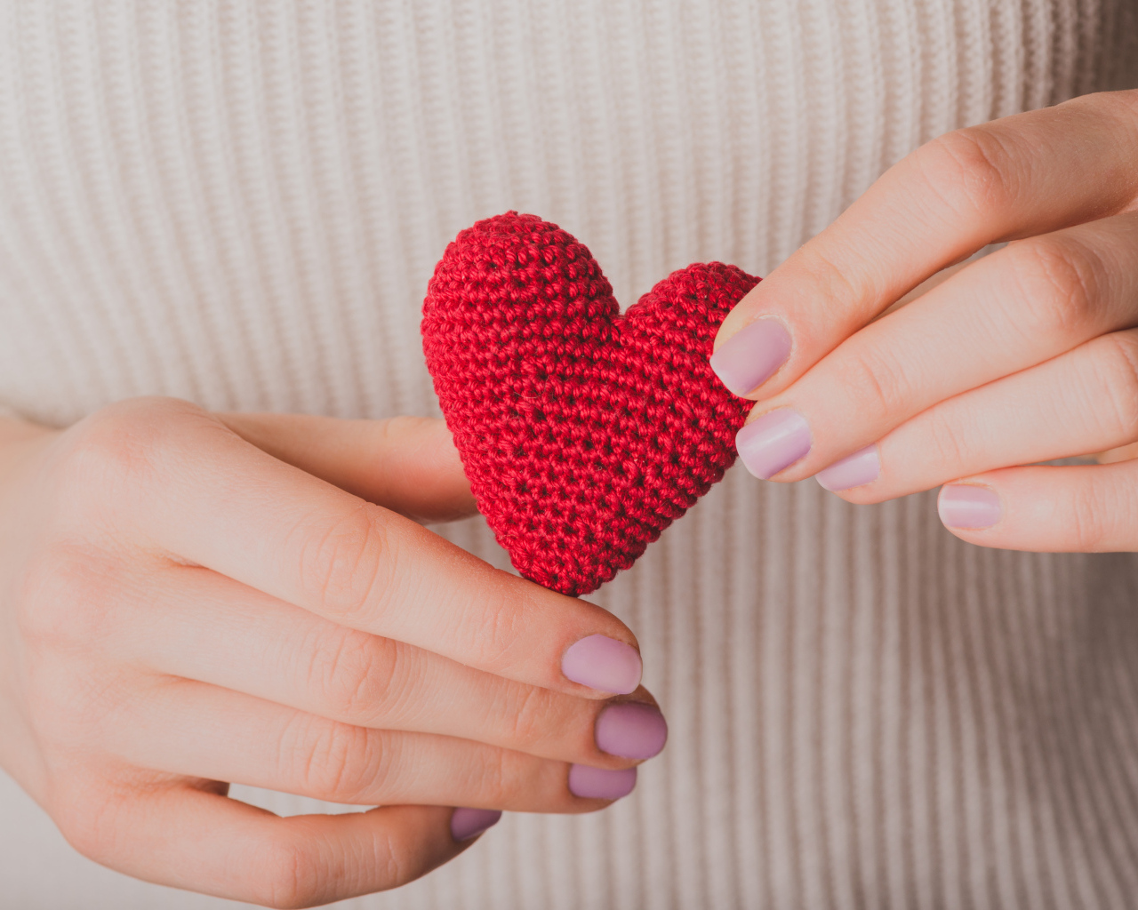 Девушка держит в руке вязаное красное сердце