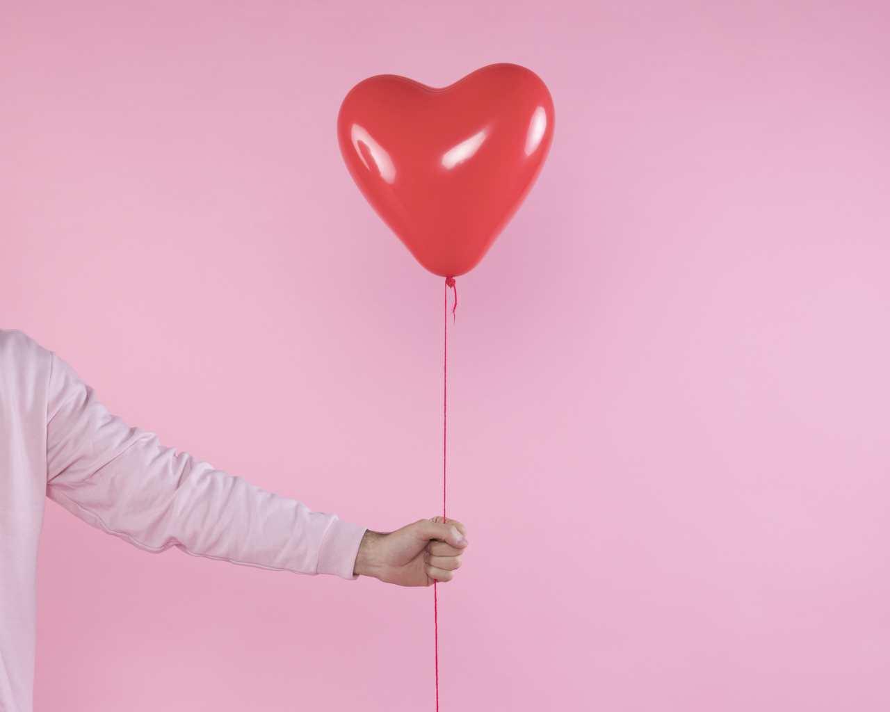 Шарик в форме сердца в руке на розовом фоне