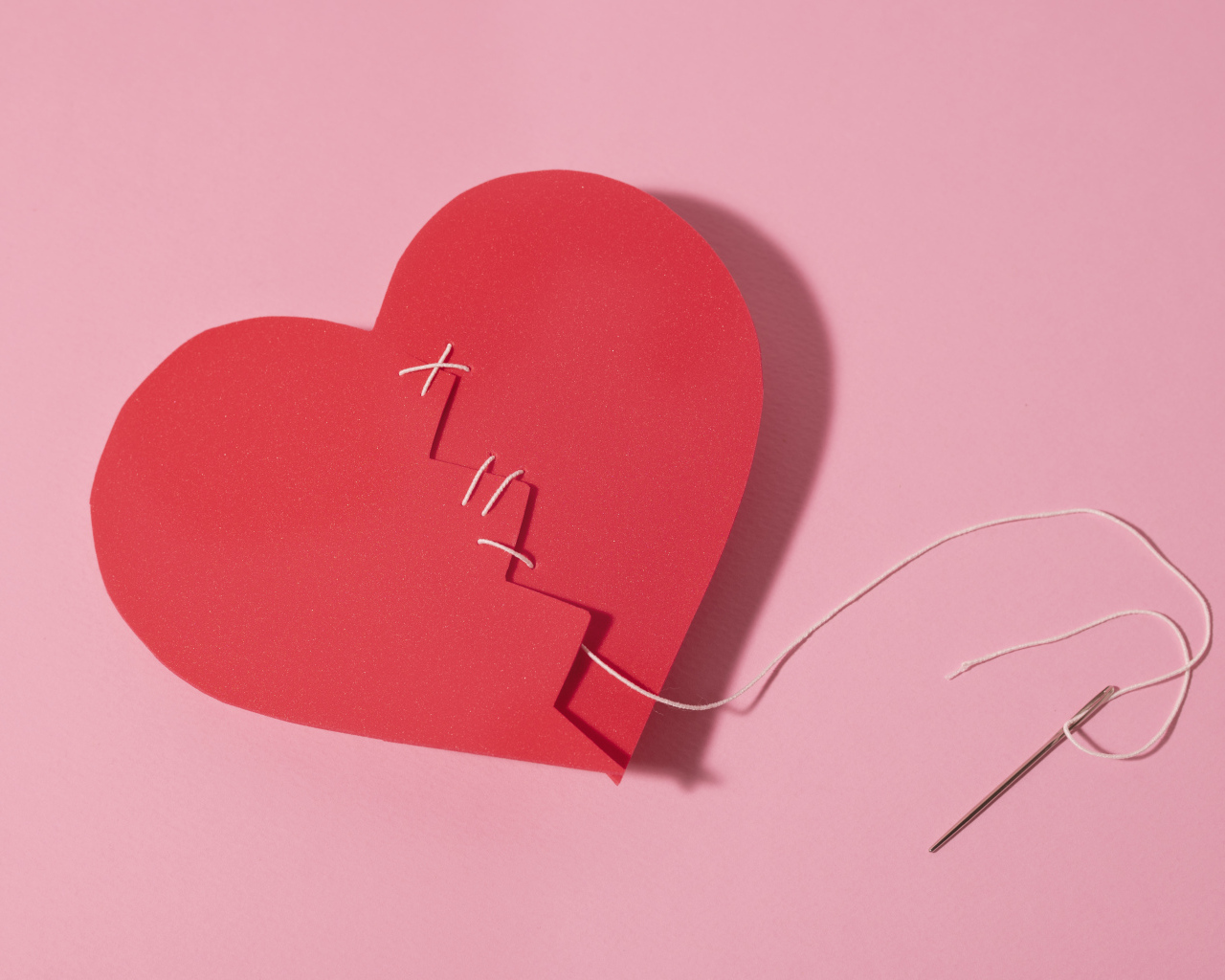 Бумажное сердце сшили нитками на розовом фоне