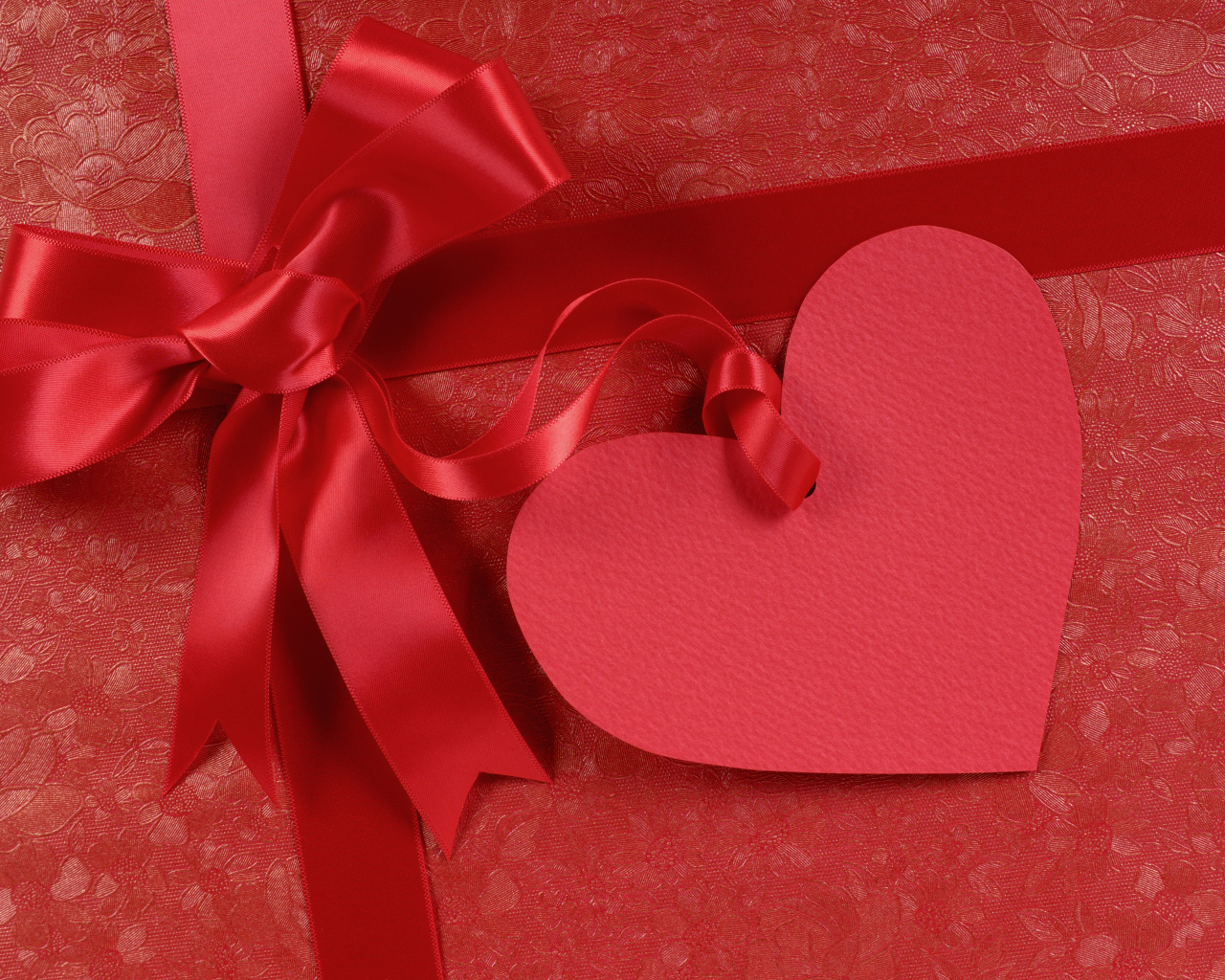 Бумажное сердце с бантом из атласной ленты на красном фоне