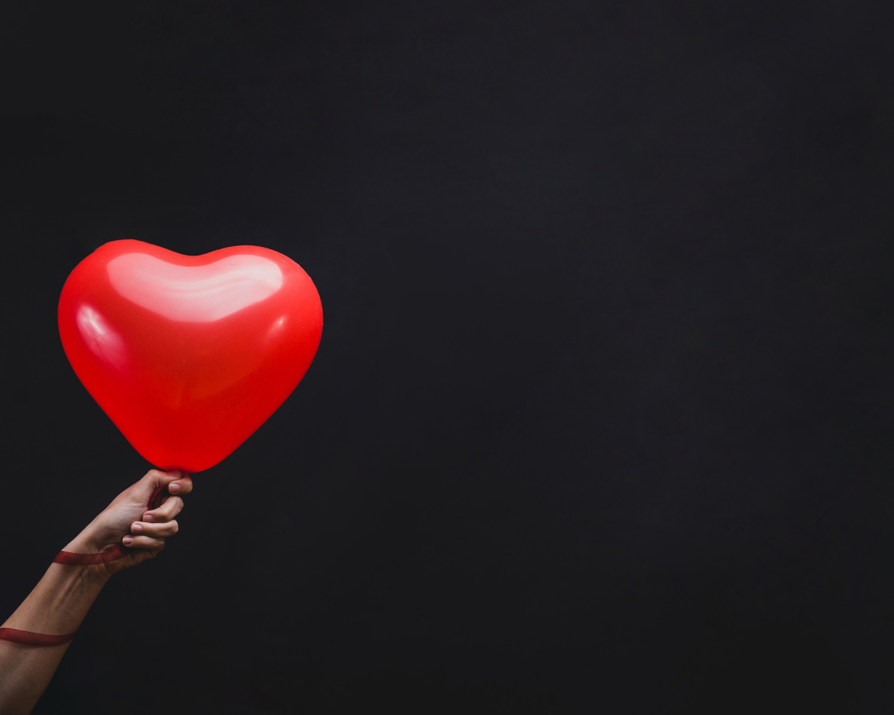 Красный шарик в форме сердца на черном фоне