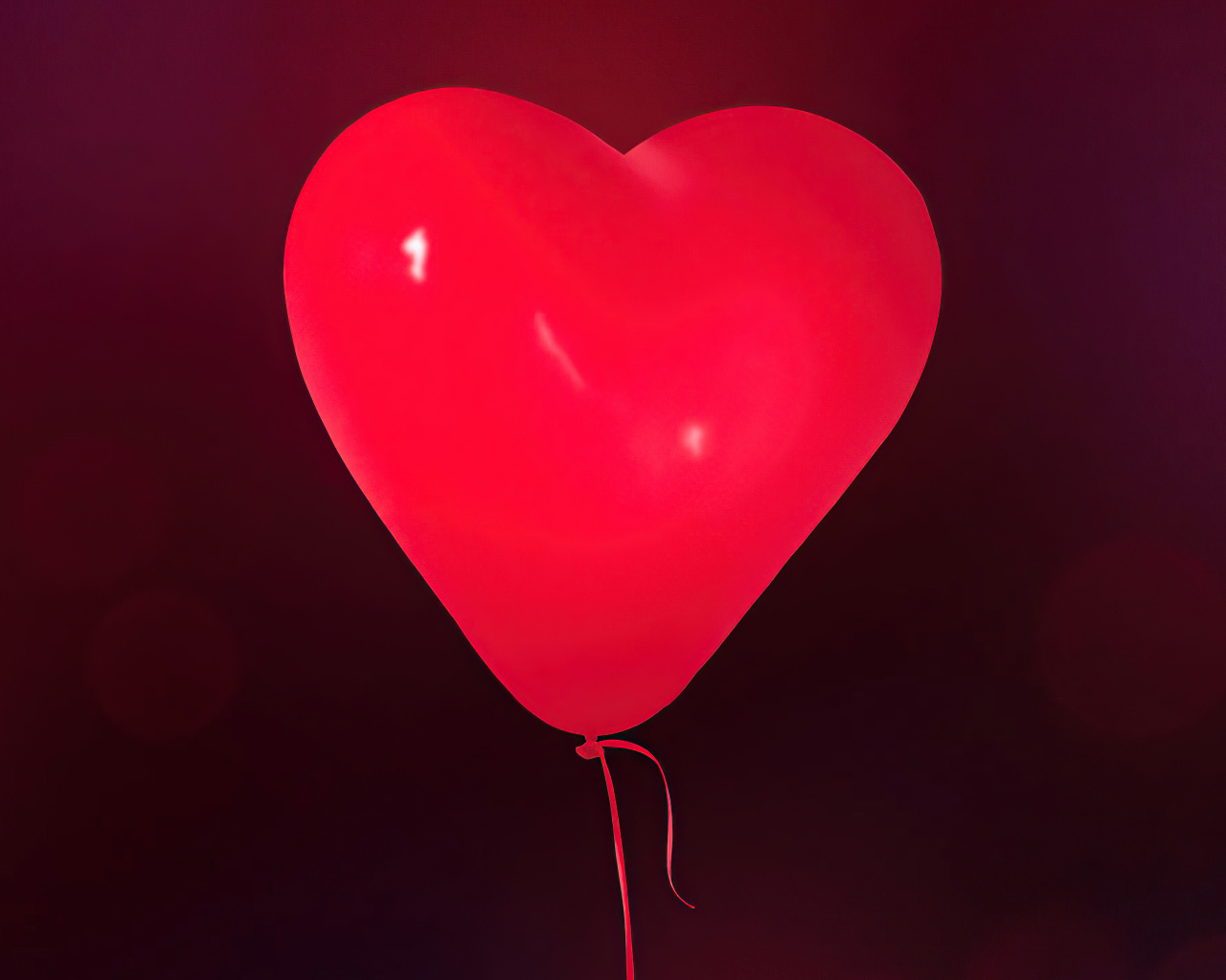 Красный шарик в форме сердца на фоне стены