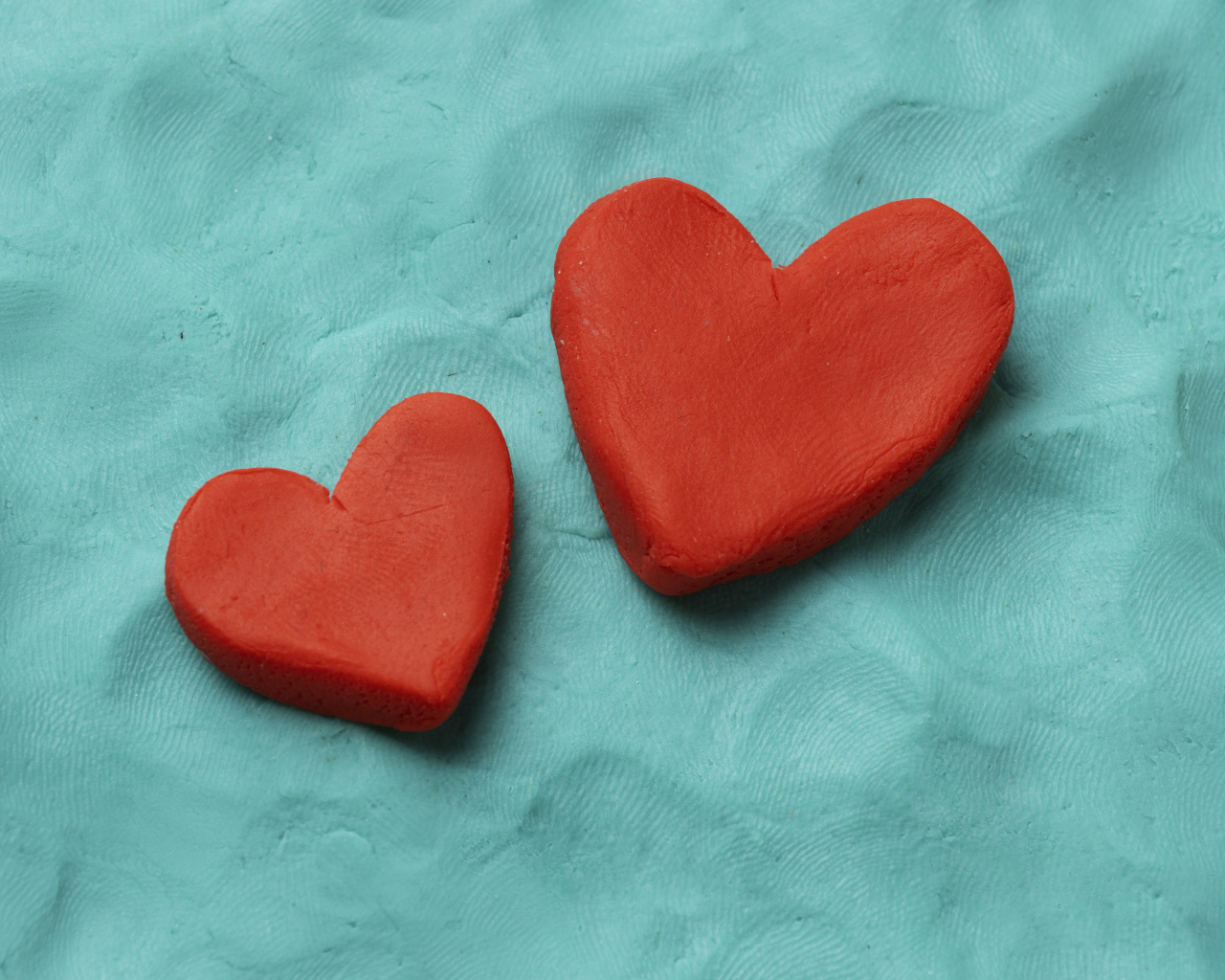 Два красных сердца из пластилина на голубом фоне