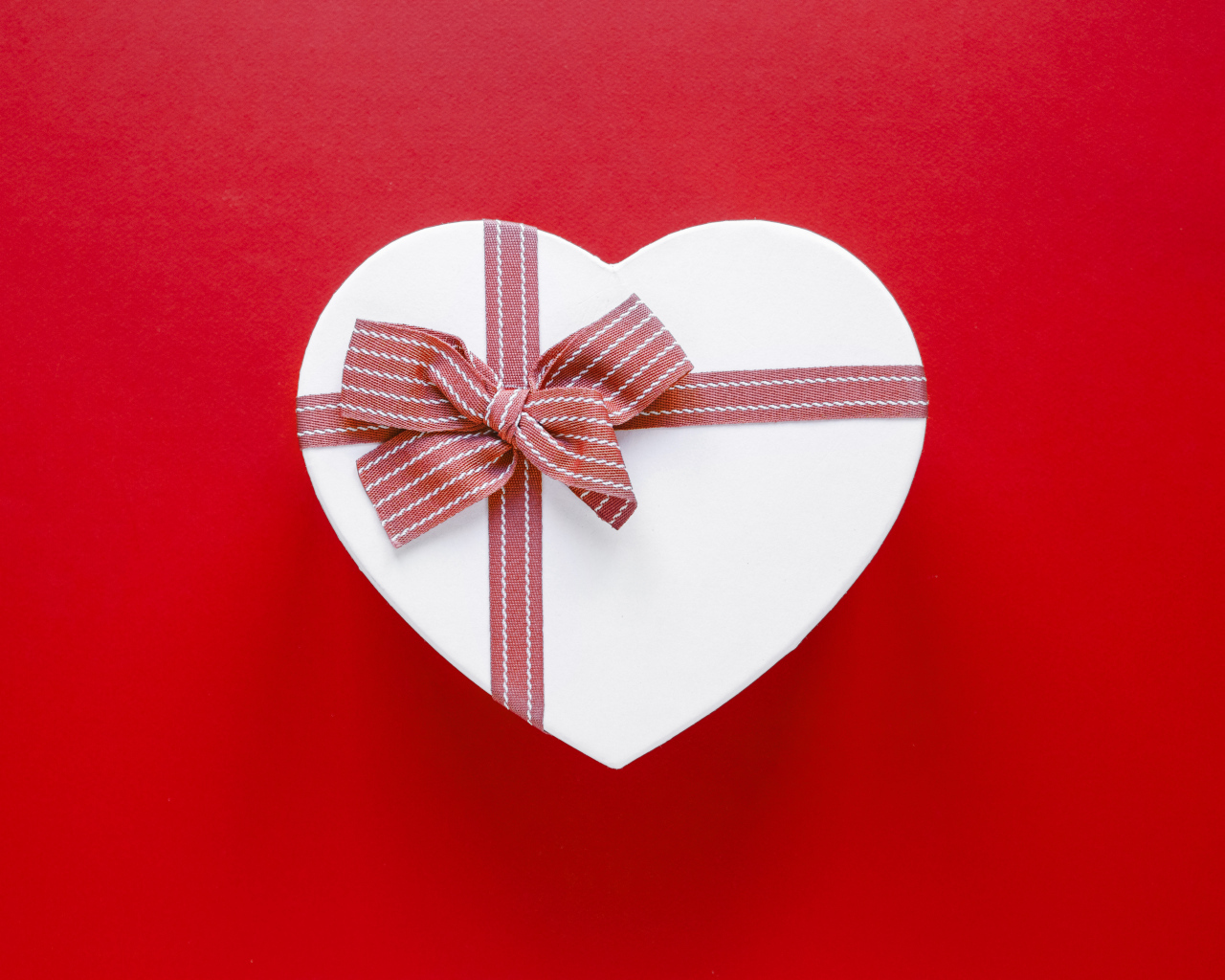 Белая коробка в форме сердца с бантом на красном фоне