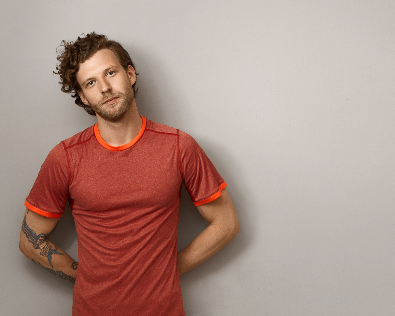 Мужчина в футболке стоит у серой стены