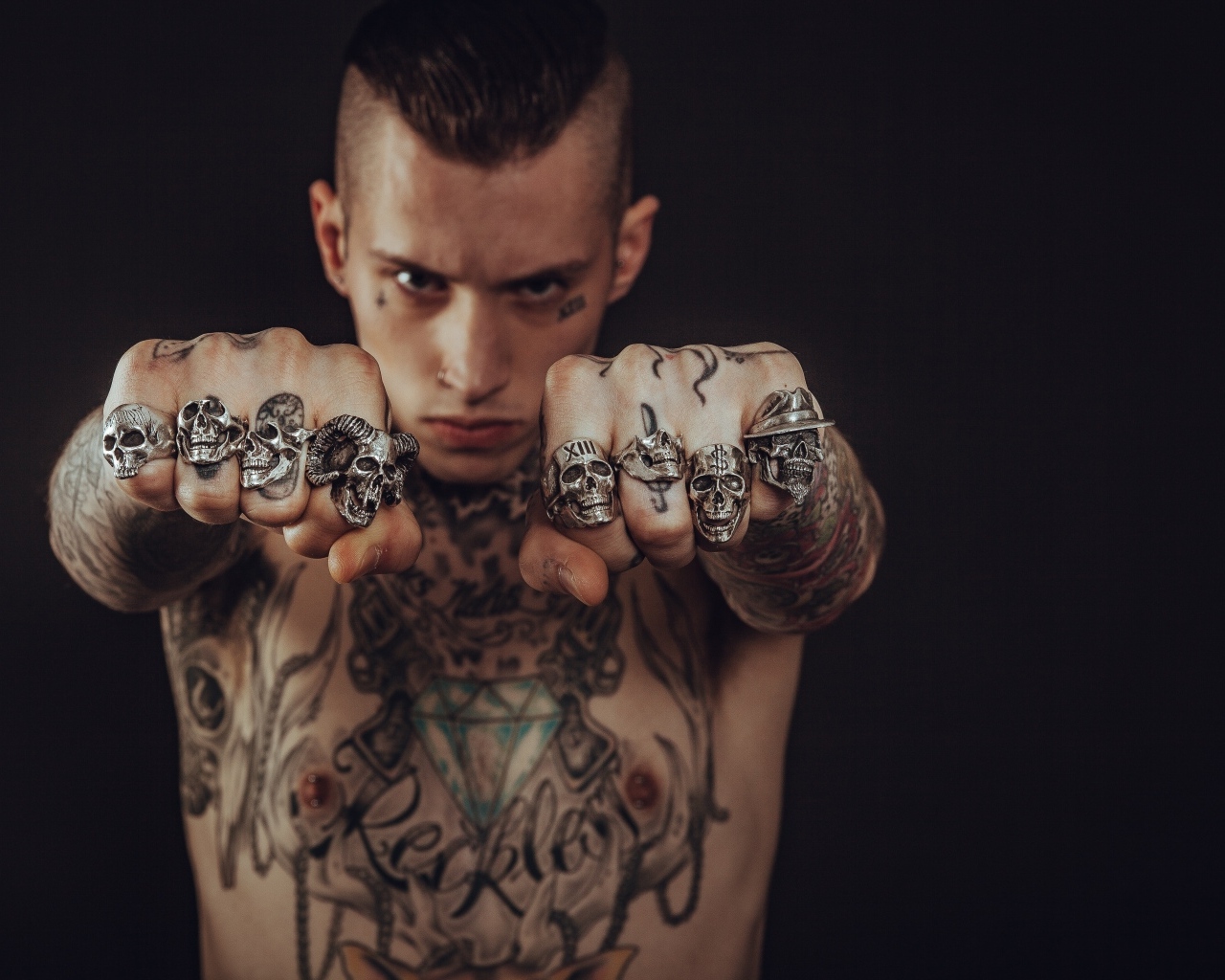 Мужчина с татуировками на теле показывает перстни на пальцах