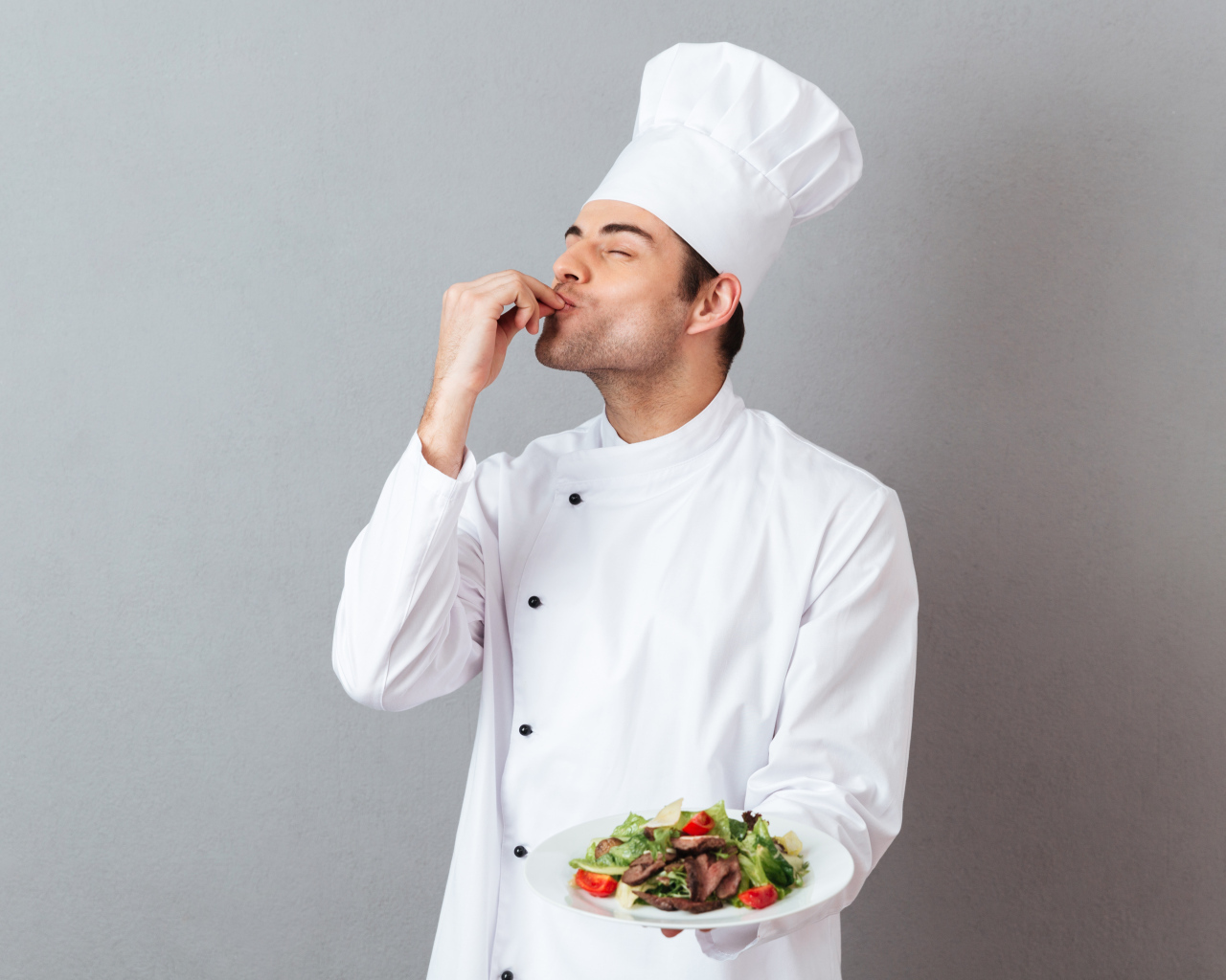 Мужчина повар в белом костюме с блюдом на сером фоне