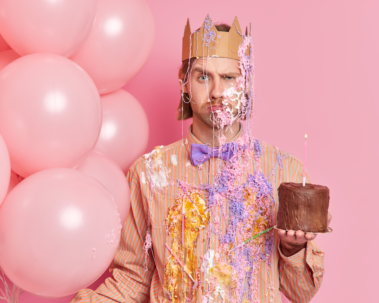 Мужчина принц с тортом и шариками на розовом фоне