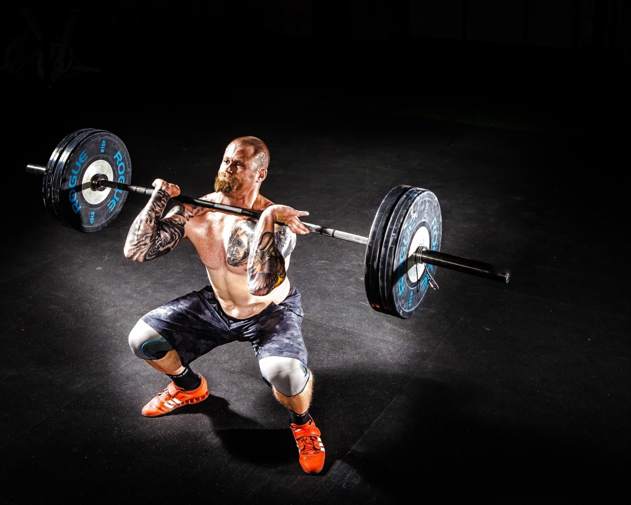 Сильный мужчина с татуировками на теле поднимает штангу