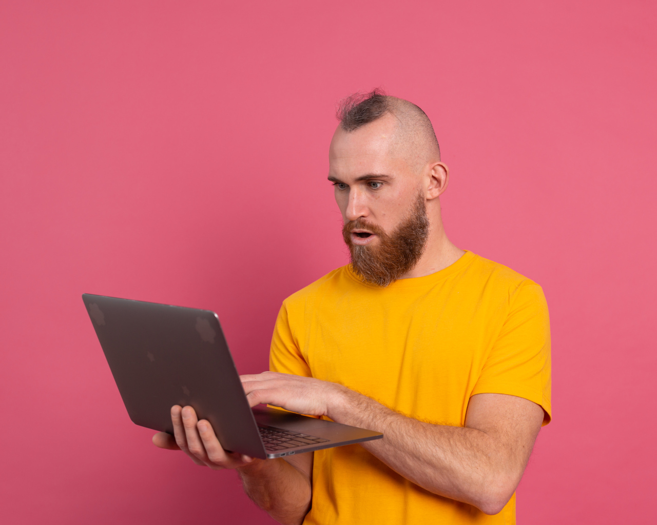 Удивленный мужчина с ноутбуком на розовом фоне