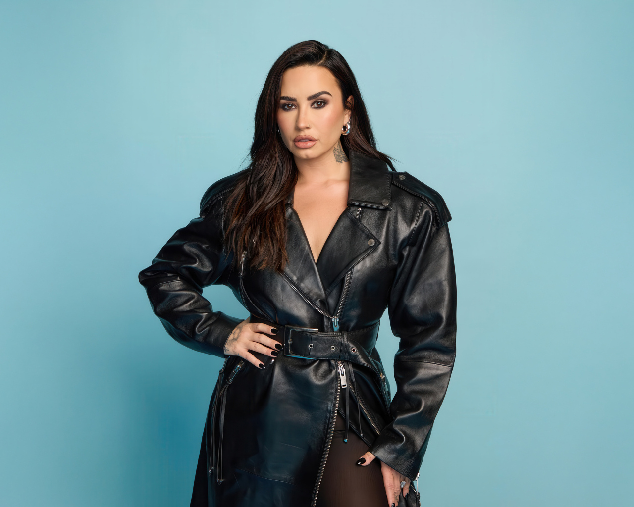 Певица Деми Ловато в кожаном черном пальто на голубом фоне