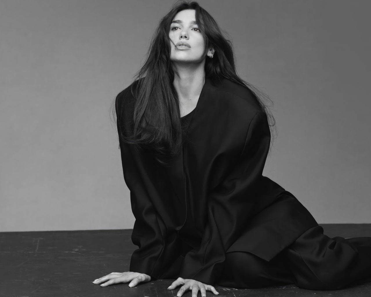 Певица Дуа Липа в черном костюме сидит на полу