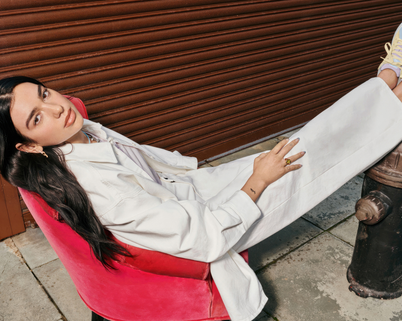 Певица Дуа Липа в белом костюме сидит в кресле