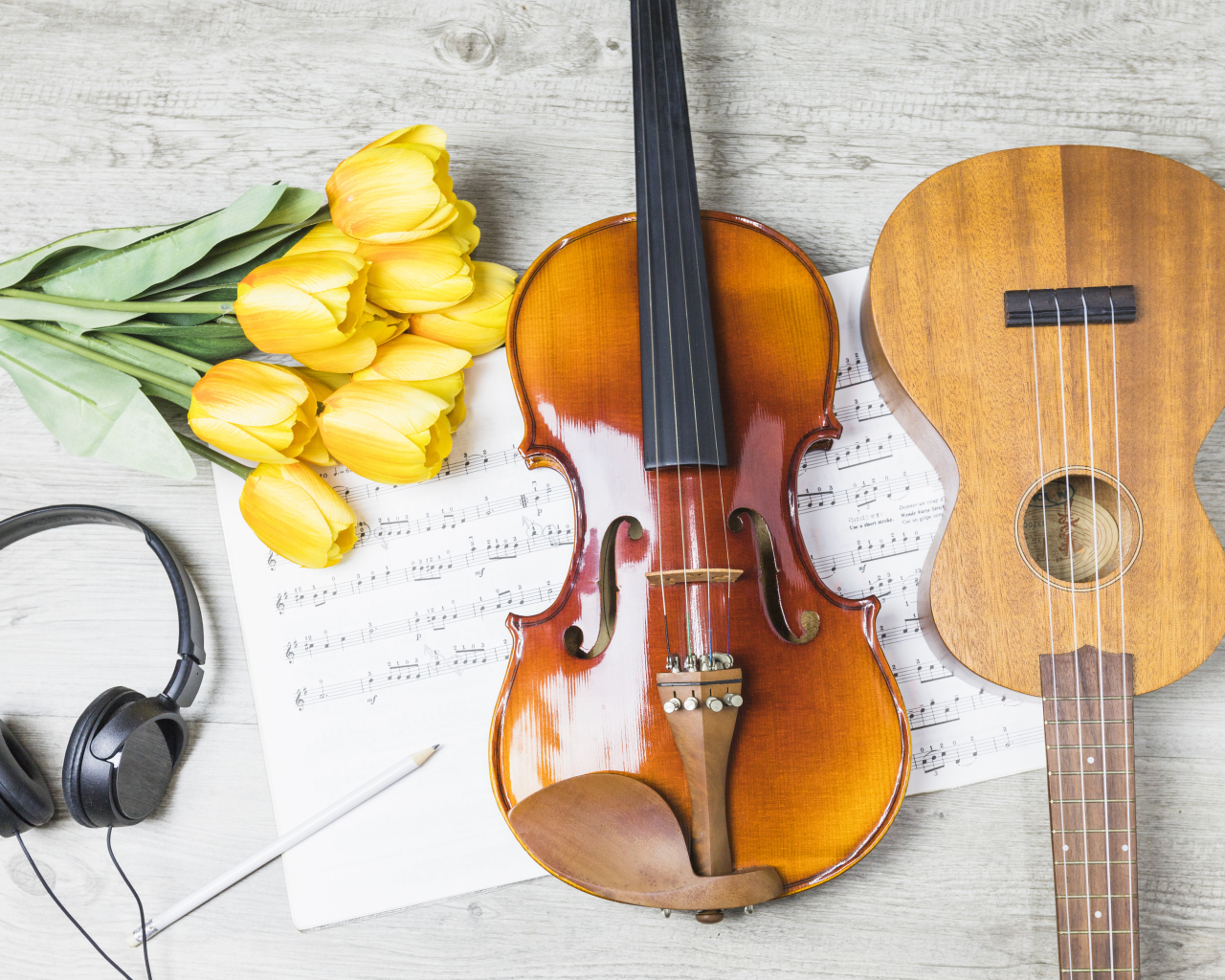 Маленькая гитара и скрипка на столе с нотами, наушниками и букетом тюльпанов
