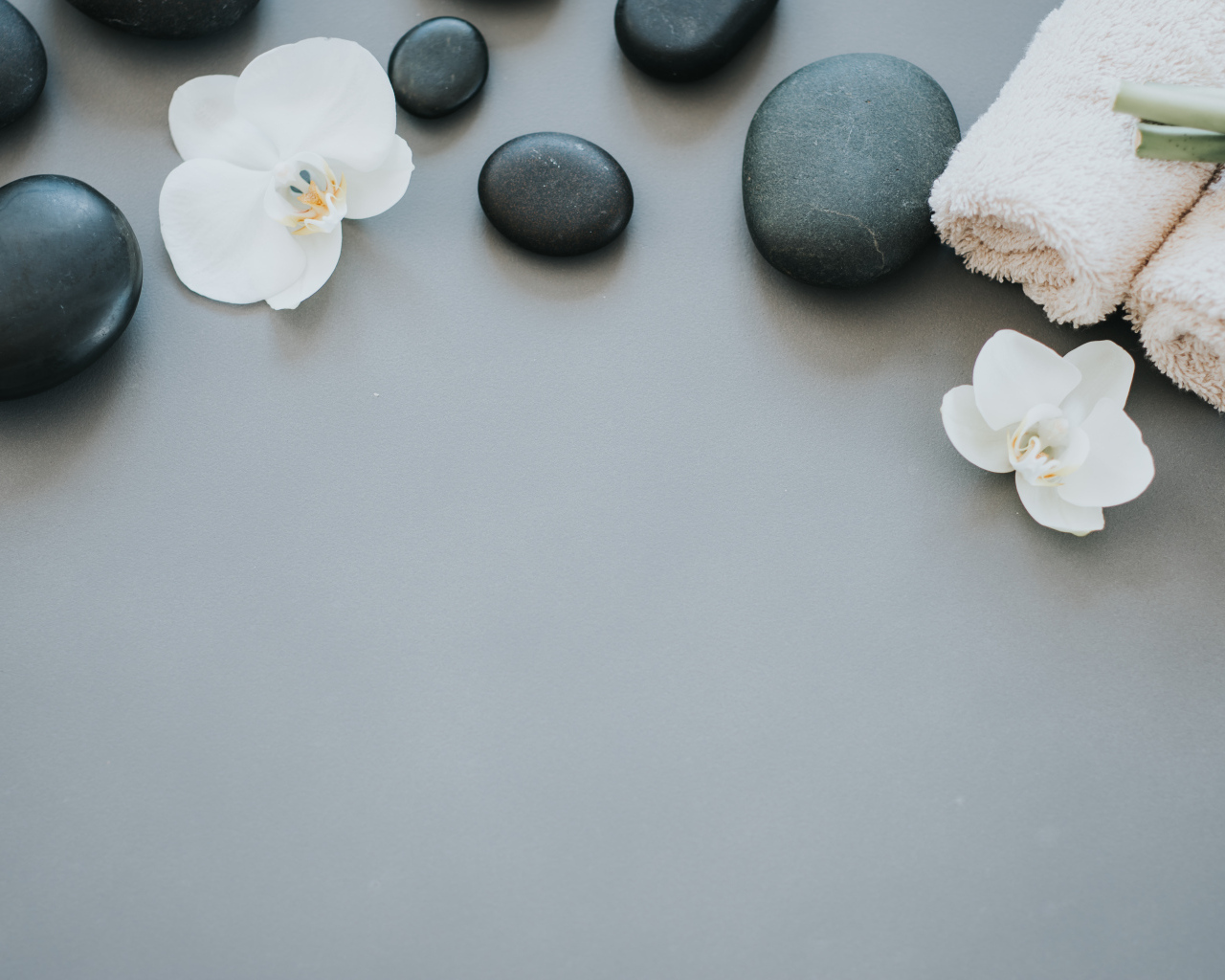 Черные камни с цветами орхидеи и полотенцем на сером фоне