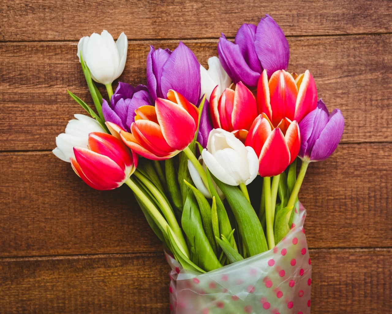 Букет разноцветных тюльпанов в пакете на деревянном фоне