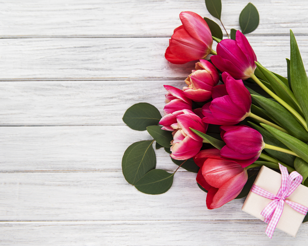 Букет розовых тюльпанов с подарком и зелеными листьями на белом столе