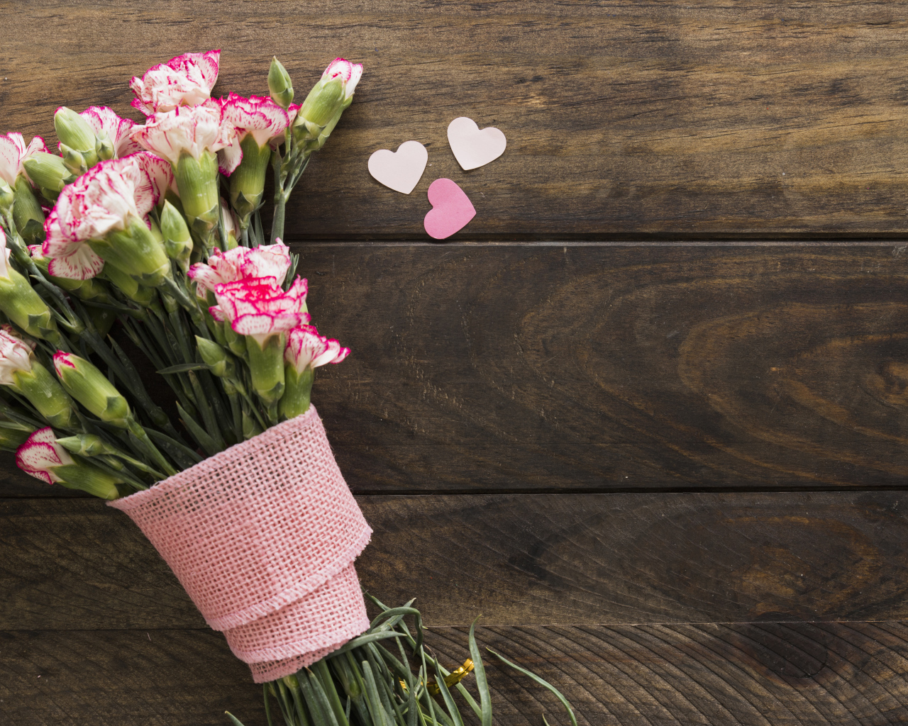 Розовые гвоздики с сердечками на коричневом деревянном фоне