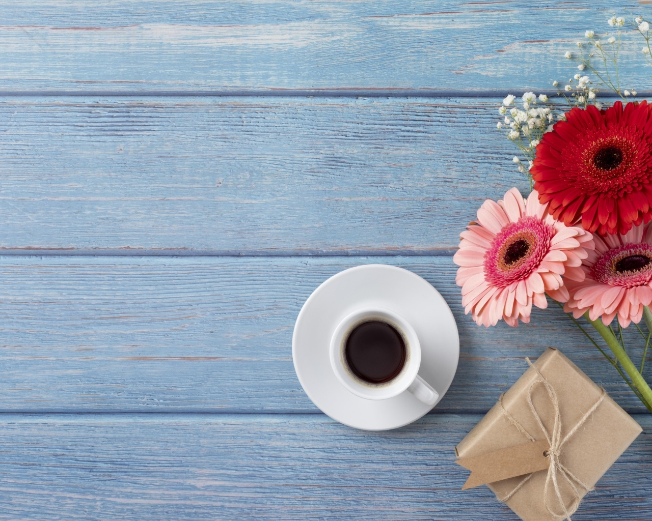 Три герберы с чашкой кофе и подарком на синем столе