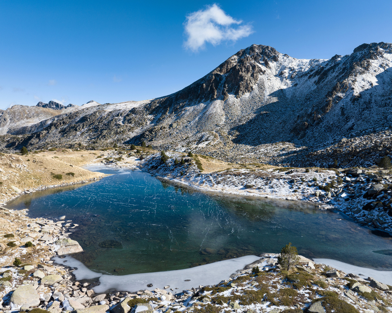 Покрытое льдом озеро в заснеженных горах в лучах солнца, Андорра