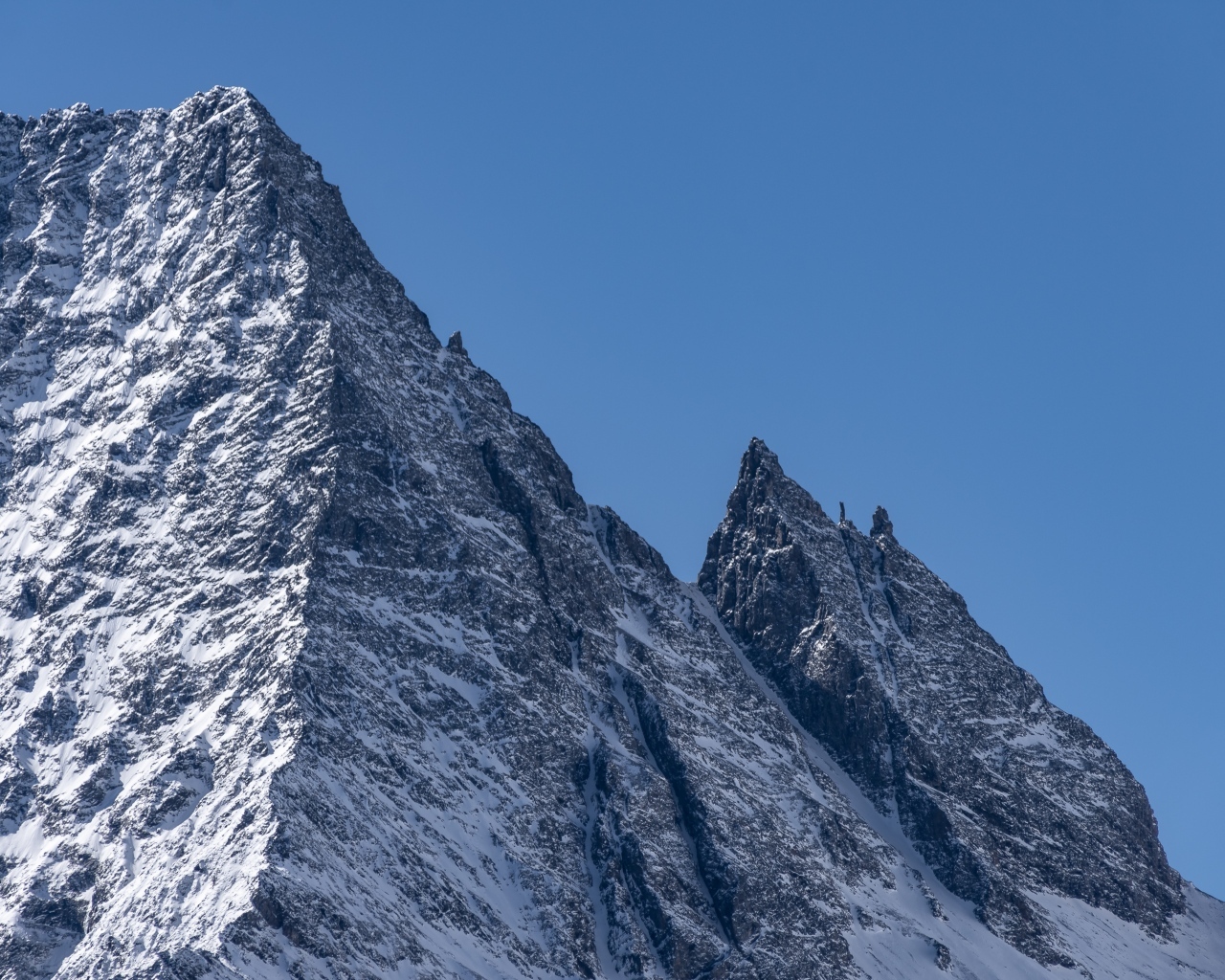 Крутая вершина горы в снегу на фоне голубого неба