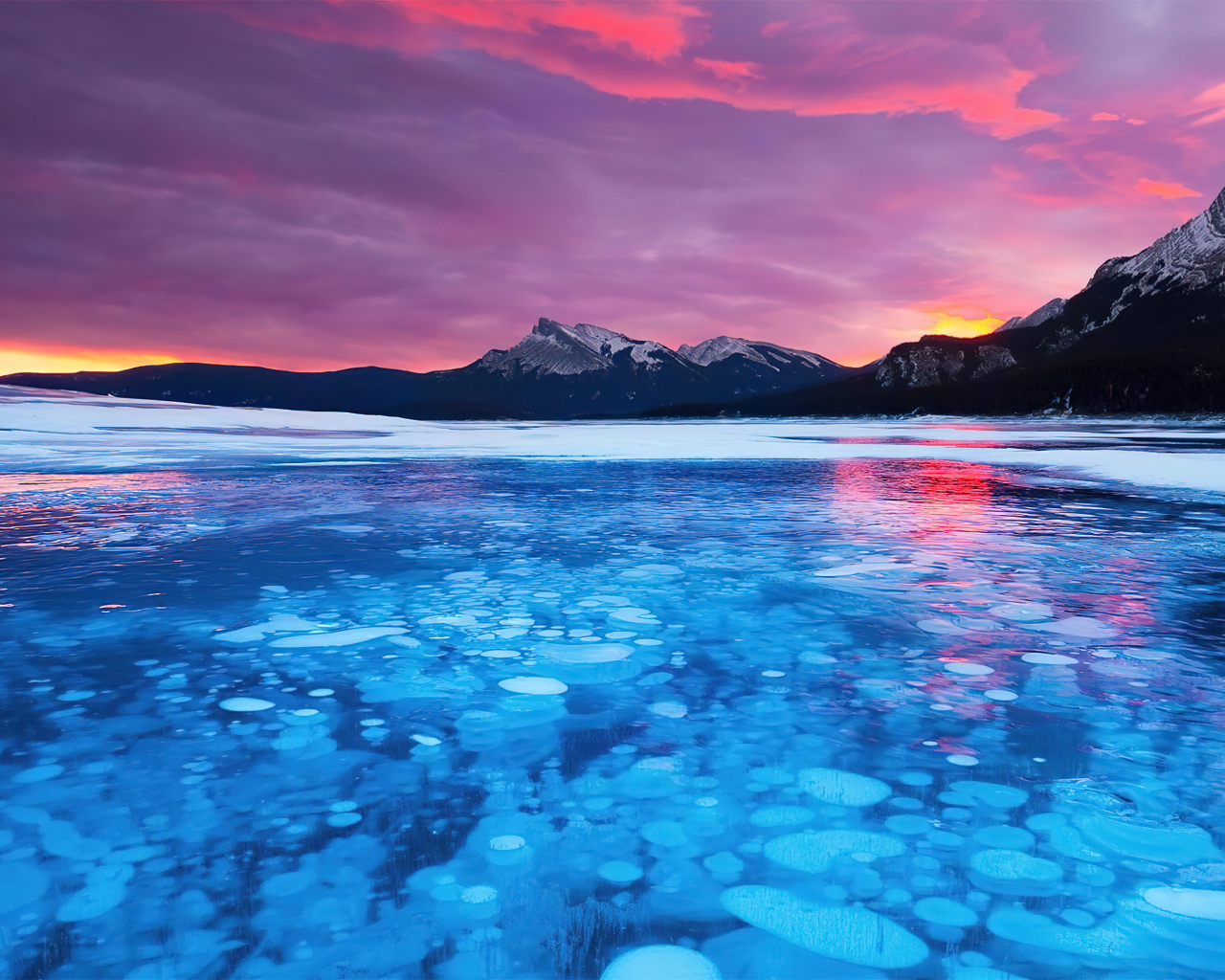 Красный закат солнца над горами у покрытого льдом озера