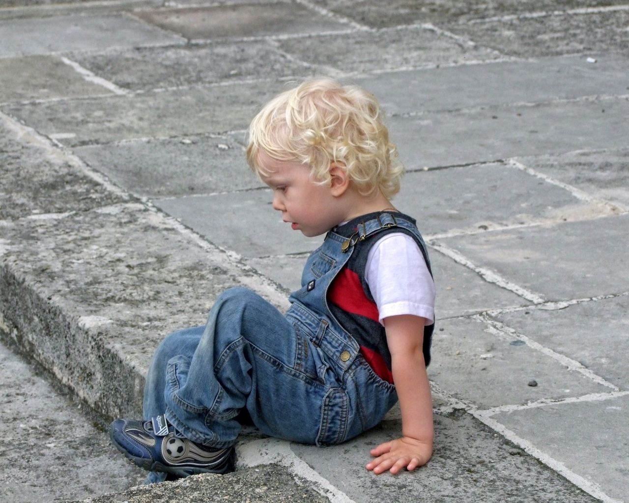 Мальчик в джинсовом комбинезоне сидит на дороге