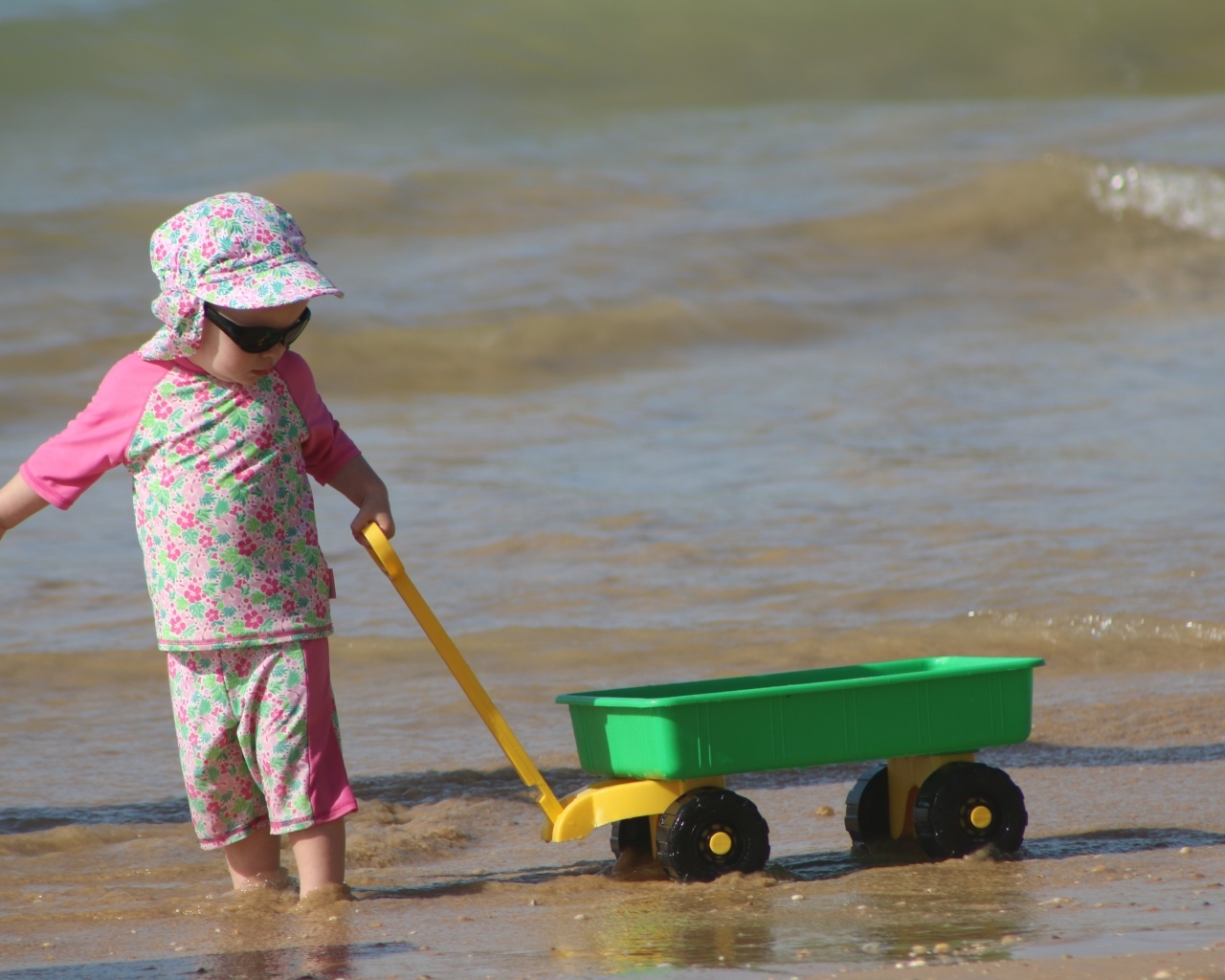Девочка с машинкой играет на песке у моря