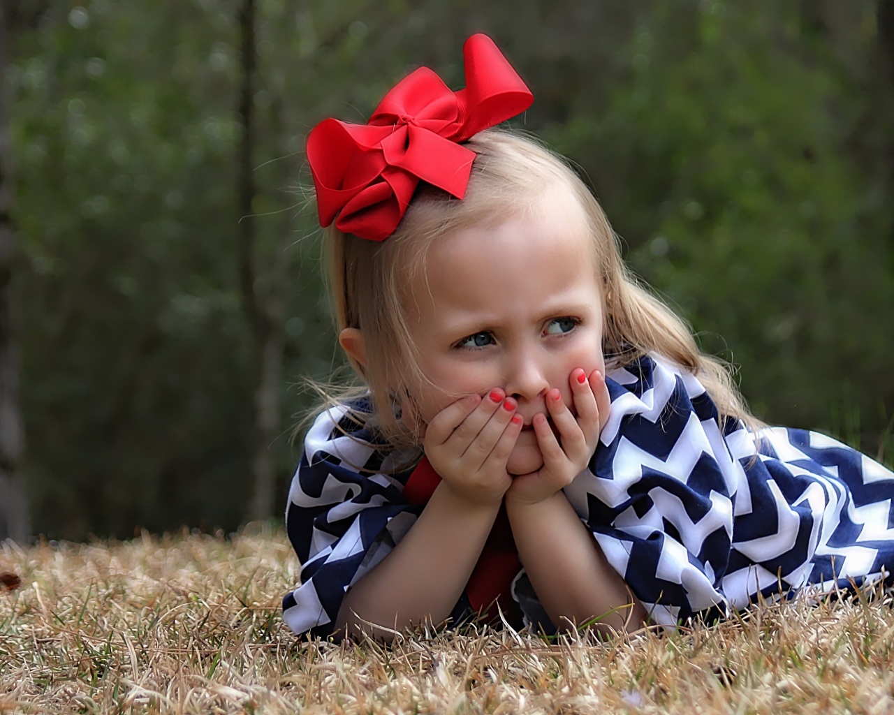 Маленькая девочка с красным бантом на голове лежит на траве